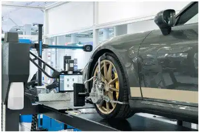 Wheel Alignment In Rancho Santa Margarita, CA At Bobby Grich Auto Repair. A car with gold alloy wheels is being aligned on a machine in a modern auto repair shop. Sensors and equipment are attached to the front wheel for alignment measurement.