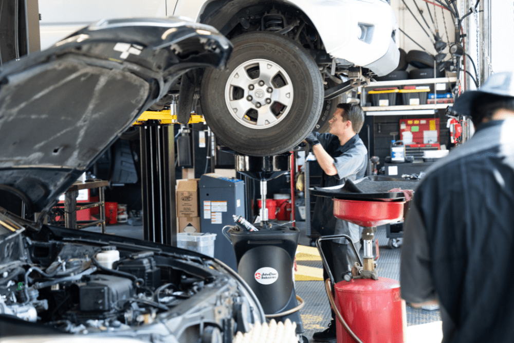 Auto repair in Rancho Santa Margarita, CA by Bobby Grich Auto Repair. Image of a technician performing an oil change on a lifted vehicle with other repairs underway in the shop. Highlighting the shop’s commitment to proper maintenance and reliable engine performance.