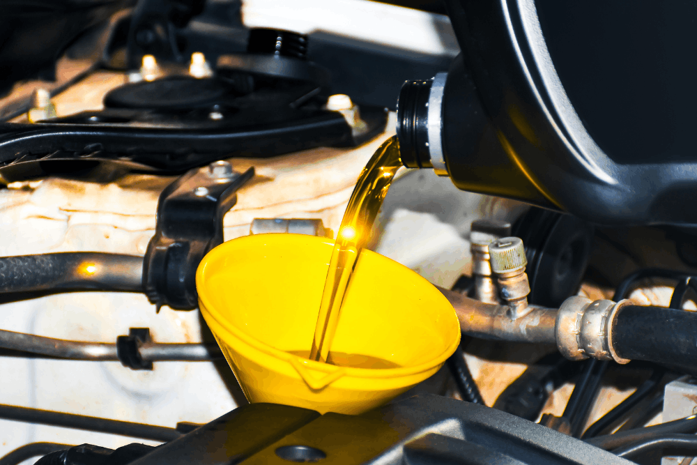 Oil change, auto repair in Rancho Santa Margarita, CA by Bobby Grich Auto Repair. Image of fresh engine oil being poured through a yellow funnel into a vehicle’s engine during routine maintenance.